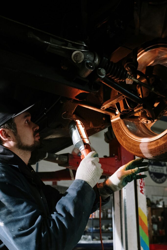 Mécanicien sous le pont élévateur effectuant une vérification du châssis au garage à Tinténiac